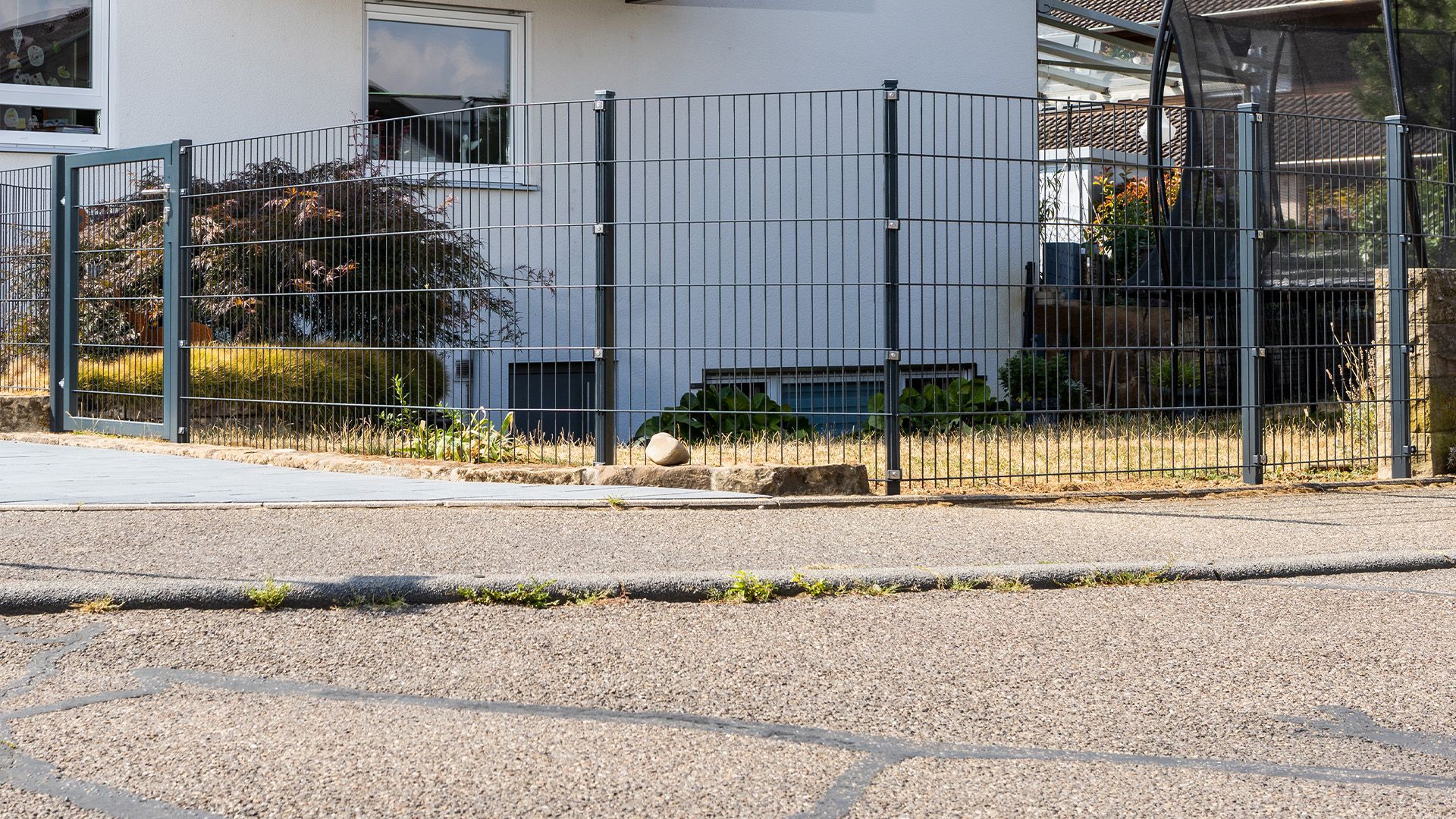 Ein Doppelstabmattenzaun an einer Straßenecke mit einem einflügeligen Tor.